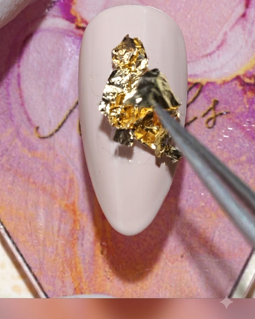 Eine Pinzette platziert ein geknittertes Stück Goldfolie auf das feuchte Gel auf einem Nagel.