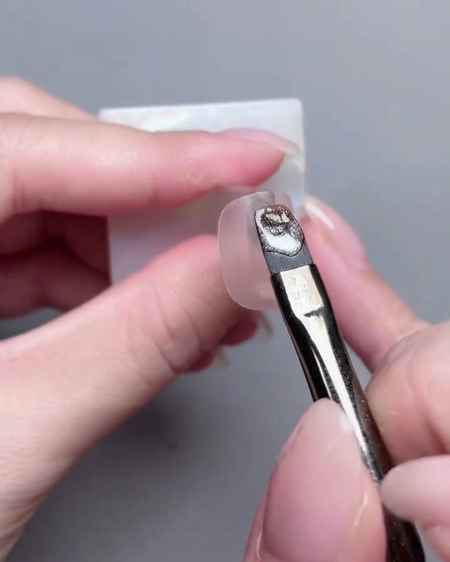 Ein Flachpinsel trägt metallisches Cat-Eye-Gel gleichmäßig über die Oberfläche der Nagelspitze auf.