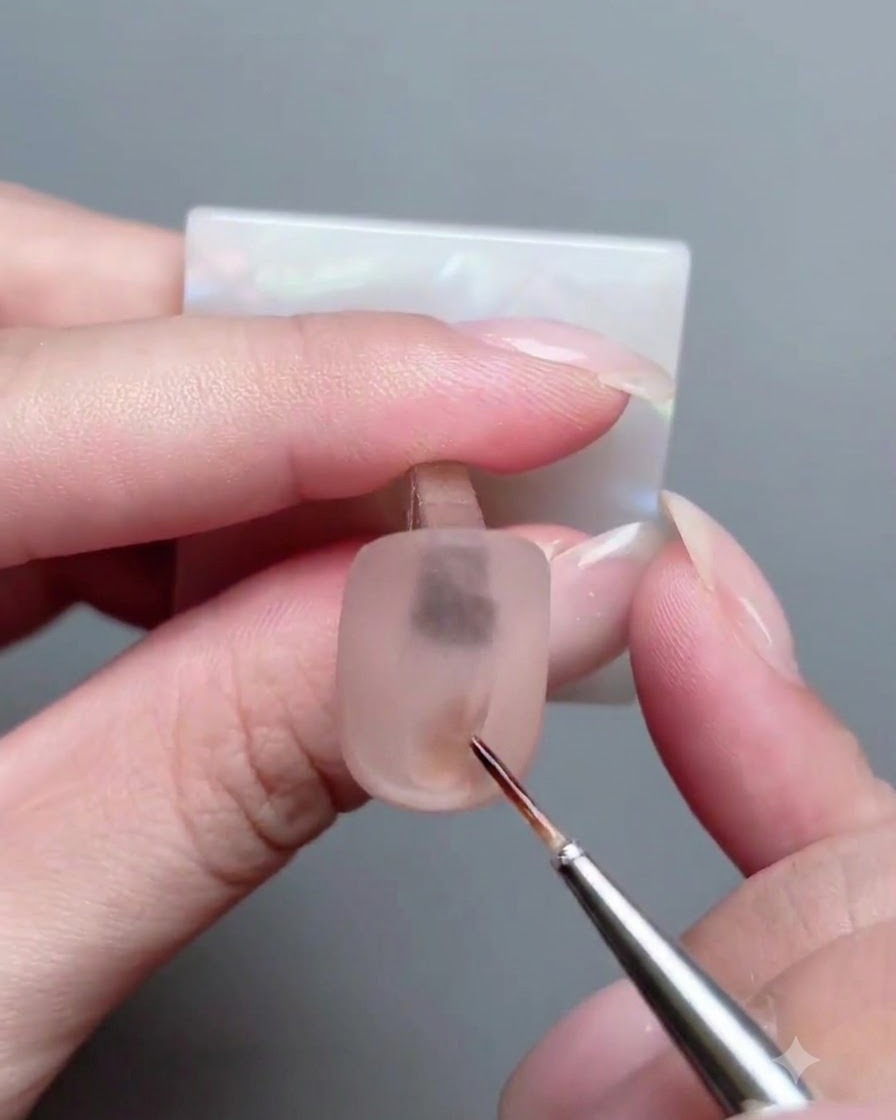 Ein feiner Detailpinsel trägt kleine Striche aus 3D-Gel auf eine matte Nageloberfläche auf.
