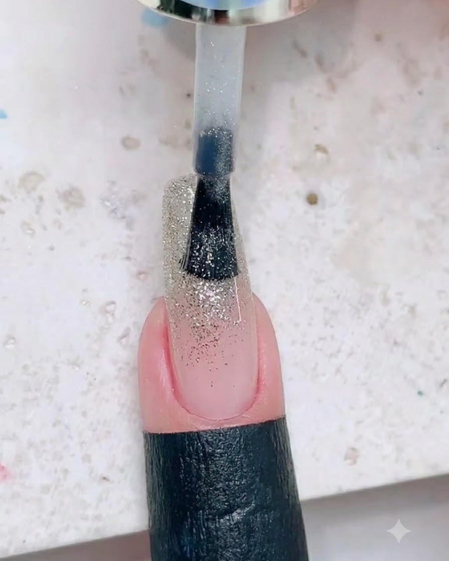Ein Lackierpinsel trägt eine dickere Schicht silbernen Glitzer auf den oberen Teil des Nagels auf.
