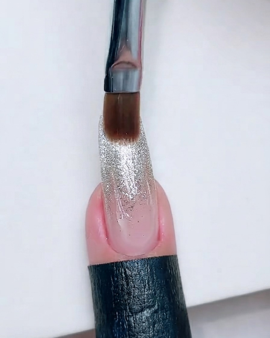 Ein sauberer Nagelpinsel ruht nahe der Kante eines Glitzer-Ombré-Nagels.