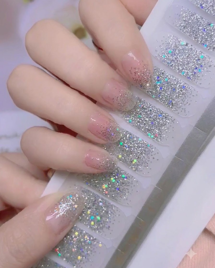 Ein Daumen drückt fest auf den Nagelhautbereich eines Silber-Glitter-Nagelfolienstickers.
