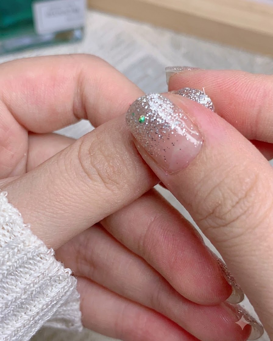 Finger ziehen den restlichen Glittersticker-Rand von einem manikierten Daumen ab.