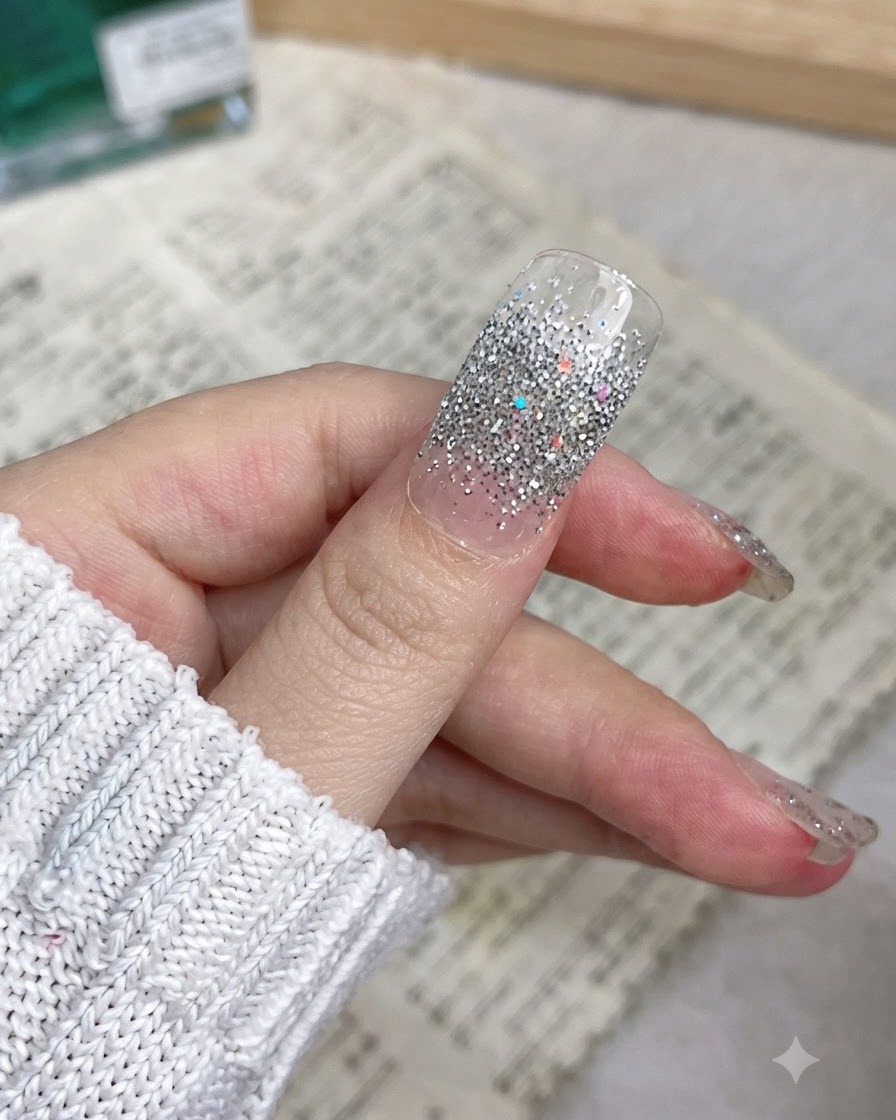 Nahaufnahme eines Daumens mit einem silbernen Glitzer Nagelaufkleber, der glatt von der Nagelhaut bis zur Kante aufgeklebt ist.