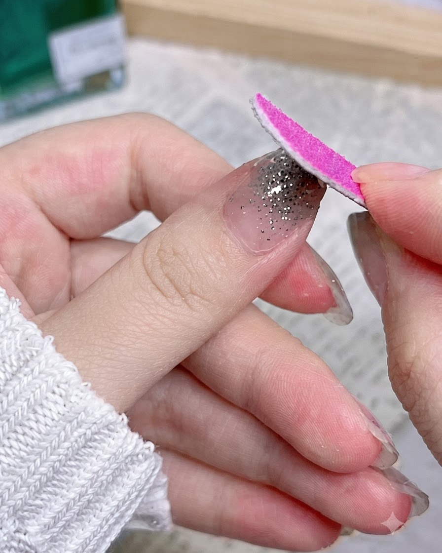 Eine rosa Nagelfeile bewegt sich nach unten entlang der Nagel kante, um überschüssiges Aufklebermaterial zu entfernen.