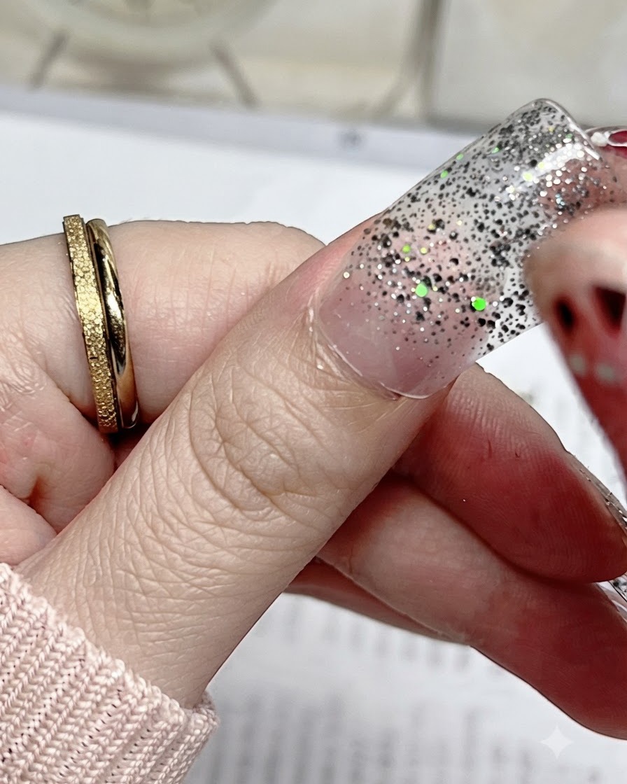 Eine Nahaufnahme eines silbernen Glitzer-Nagelstickers, der präzise an der Nagelhaut eines natürlichen Daumennagels ausgerichtet wird.