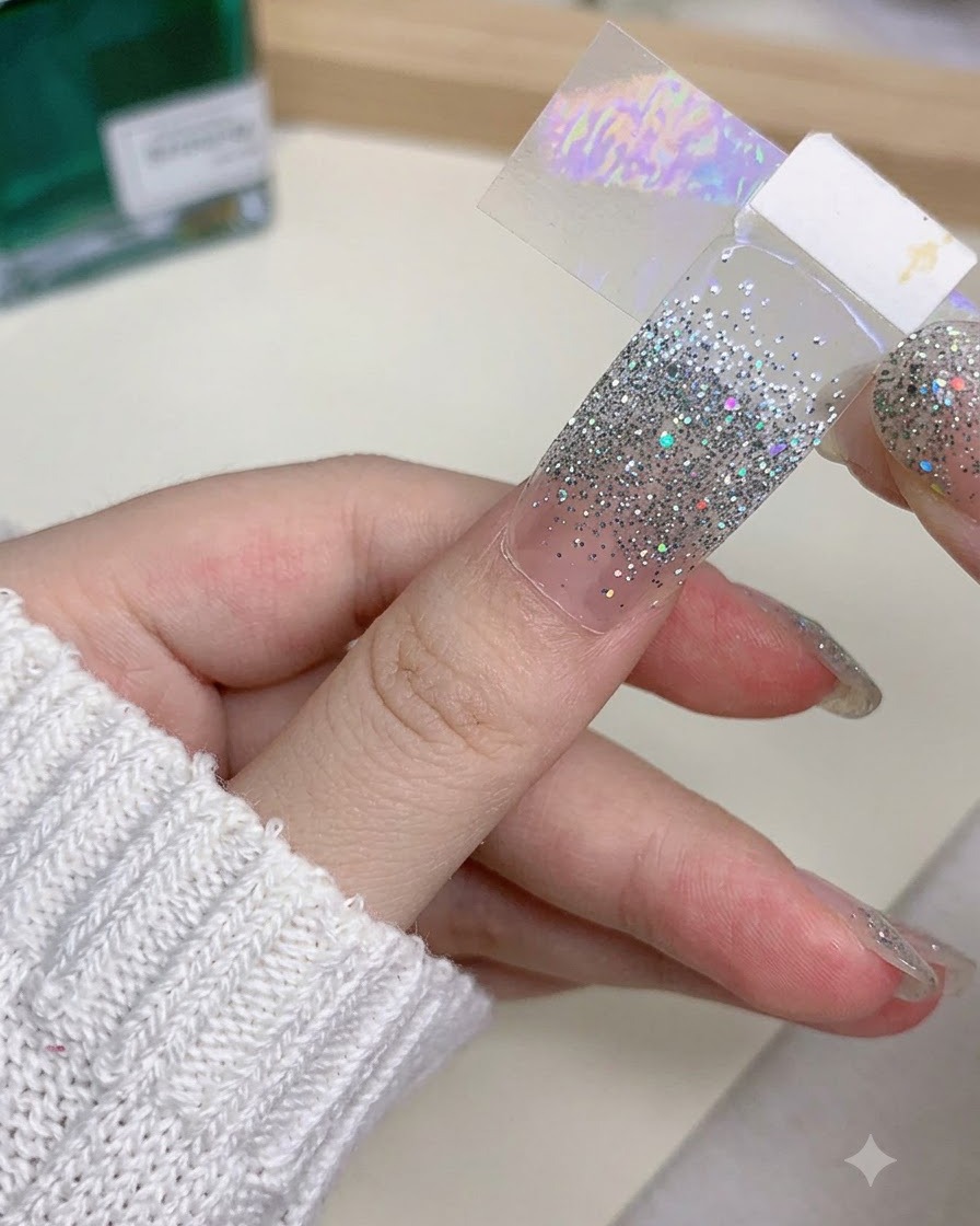 Nahaufnahme einer Hand, die einen künstlichen Nagel hält und vorsichtig mit einem Feilwerkzeug anpasst.