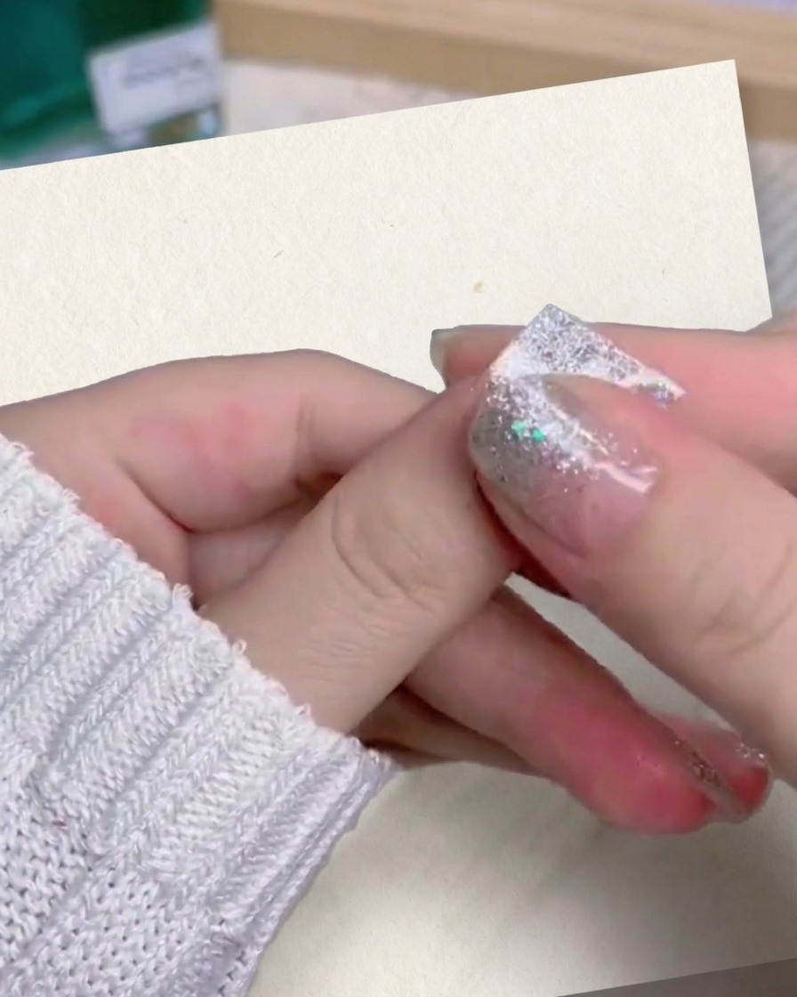 Nahaufnahme von Daumen und Zeigefinger beim festen Andrücken eines Silber-Glitter-Kunstnagels.
