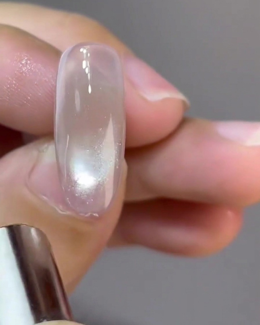 Ein kleiner runder Magnet formt eine reflektierende Glaskugel-Cat-Eye-Spiegelung auf einem Nagel.