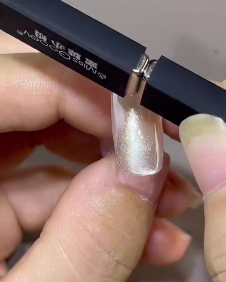 Zwei Magnete werden in einem Winkel über einem Fingernagel gehalten und ziehen den Cat-Eye-Lack in ein schwebendes Band.
