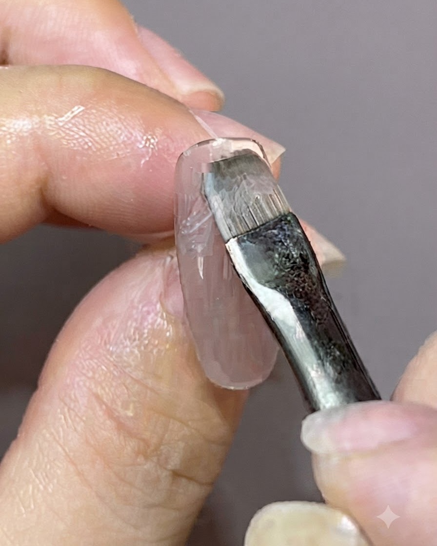 Ein Detailpinsel trägt eine frische Schicht Gellack über ein bereits bestehendes magnetisches Nageldesign auf.