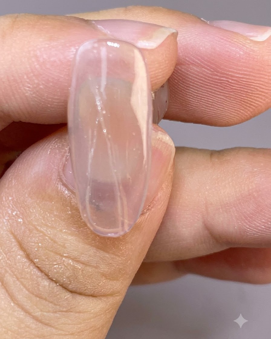 Eine Nahaufnahme eines klaren Nagels mit feinen, zarten gemalten Federlinien, die über die nasse Oberfläche gezogen wurden.