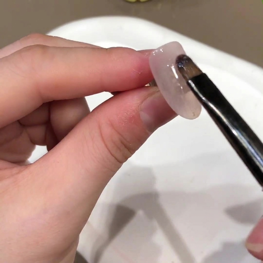 Ein Nagelpinsel trägt eine nude-rosa Gel-Basisfarbe auf die Oberfläche eines künstlichen Nagels auf.