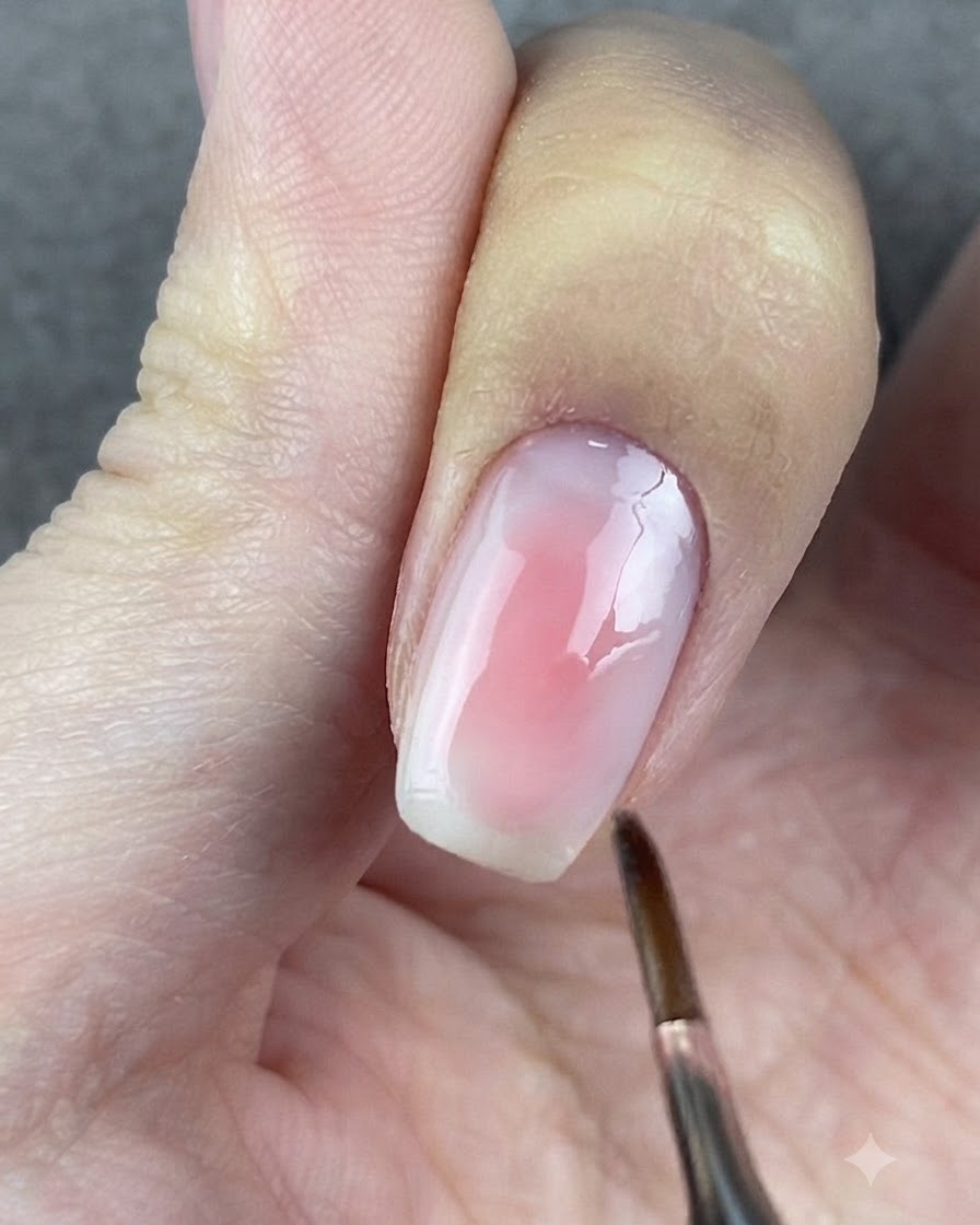 Ein runder Pinsel tupft sanft auf die Ränder des Rosagels auf einem Fingernagel.