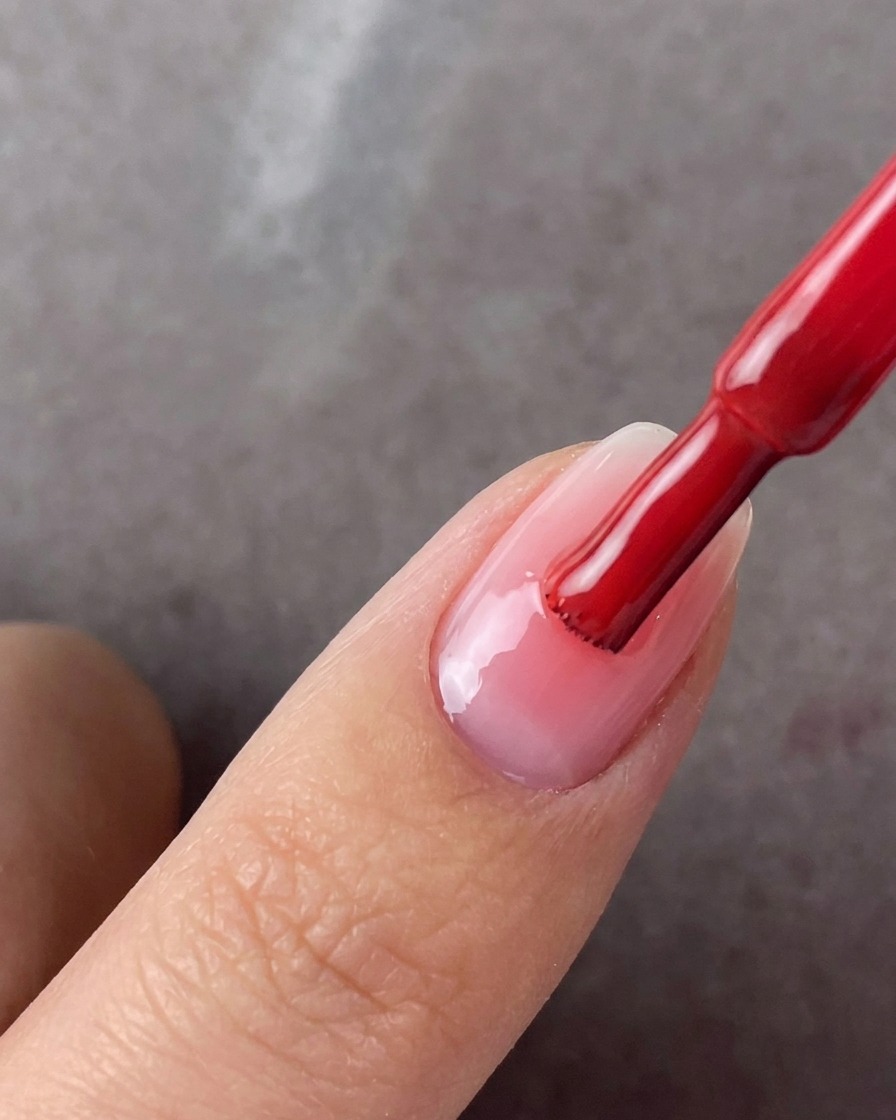 Ein Pinsel trägt eine zweite Schicht Rosagel auf die Mitte eines manikürten Nagels auf.
