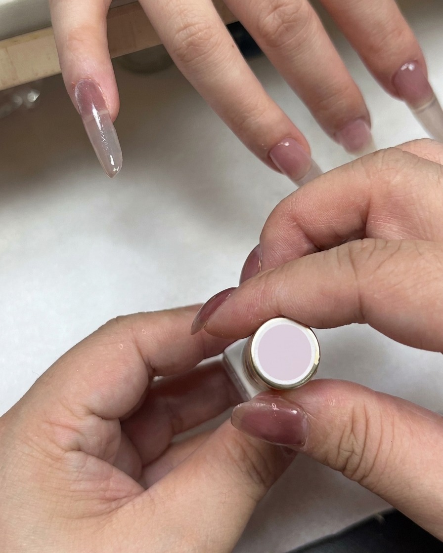 Ein Nagellackfläschchen mit hellrosa Kappe wird in der Nähe einer Hand mit Farbverlaufsnägeln gehalten.