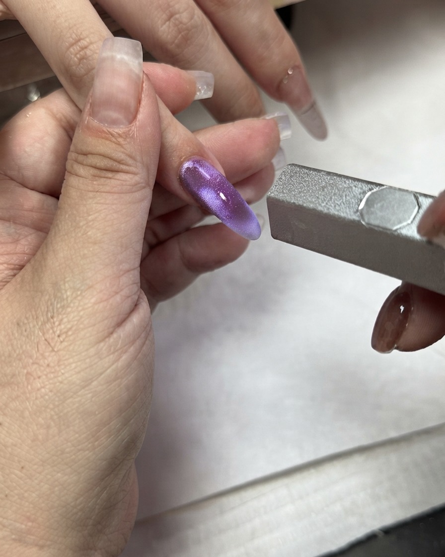 Ein Magnetstab wird über einem lila Cat-Eye-Farbblock auf einem Zeigefinger verwendet.