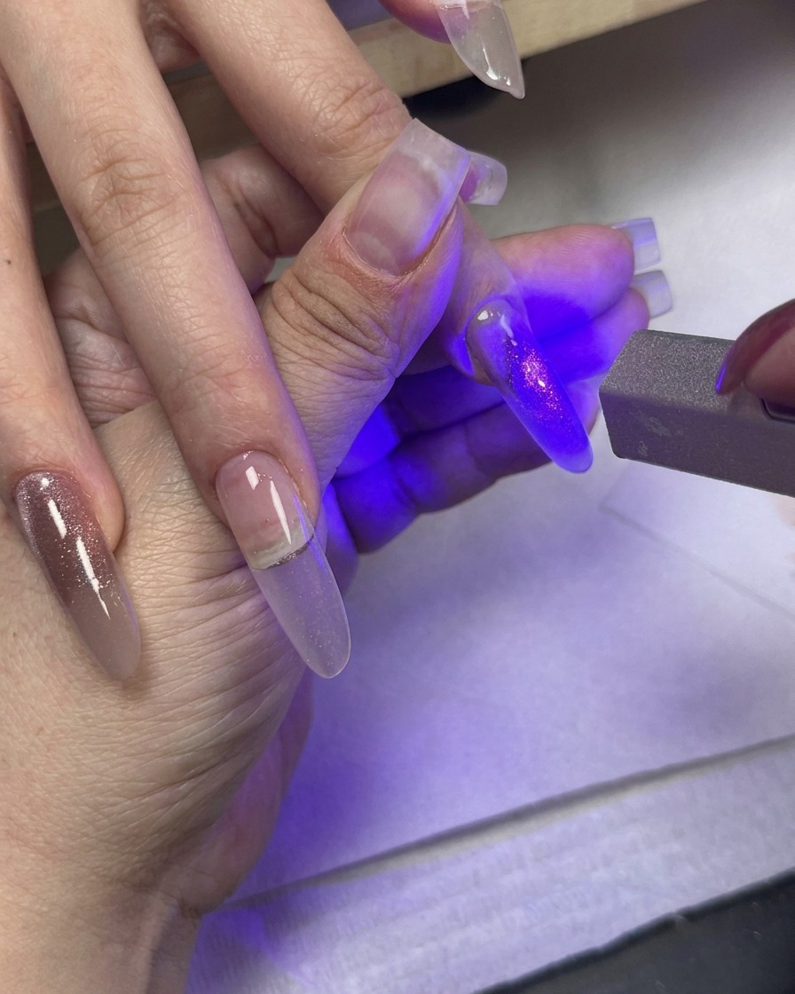 Ein UV-Licht härtet einen lackierten Nagel aus, während andere Finger mit Cat-Eye-Gel-Farbverlauf in der Nähe ruhen.