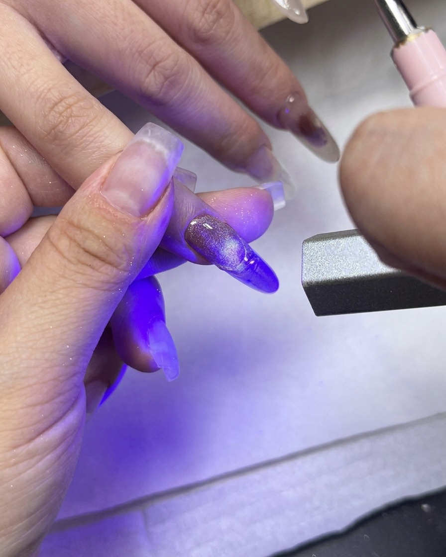 Eine UV-/LED-Härtungslampe ist direkt auf den Mittelfinger gerichtet und zeigt die strukturierte French Spitze.