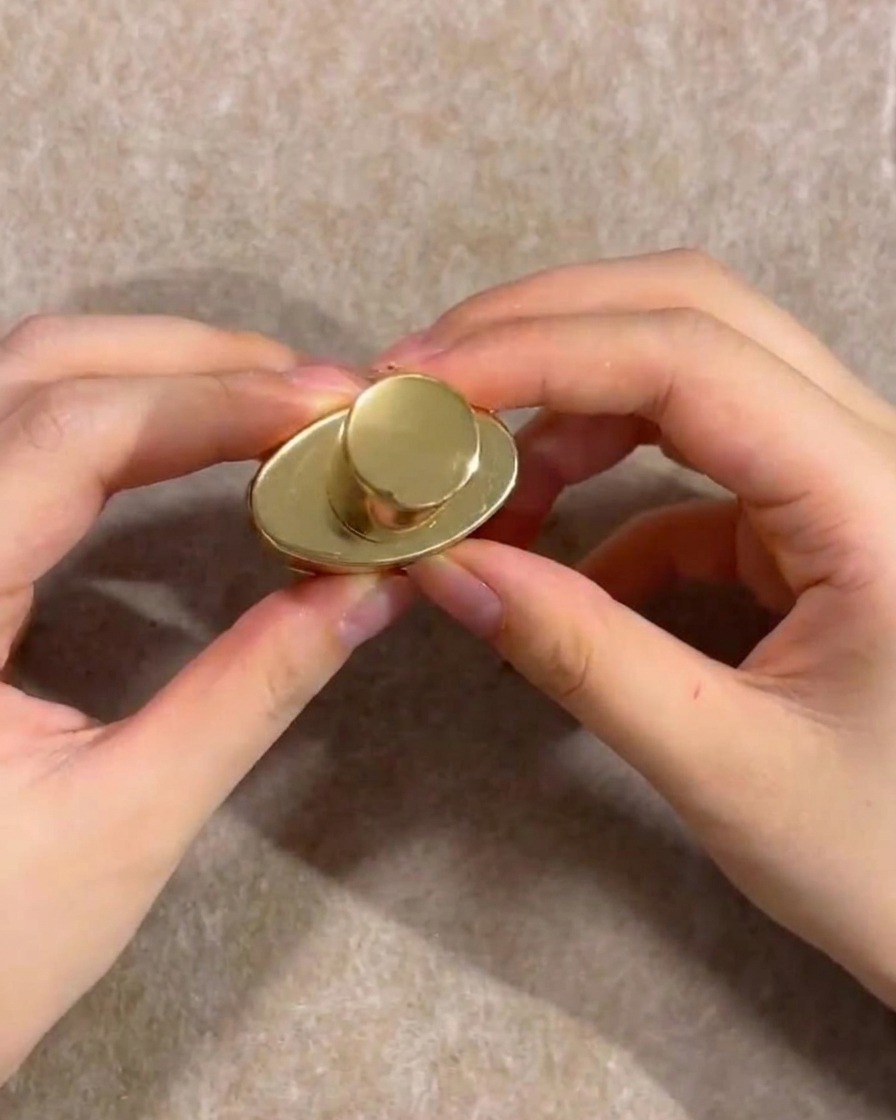 Hände halten die goldene Kappe einer Nude-Gel-Nagellackflasche.