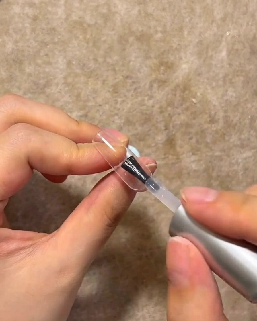 Ein Nagelpinsel trägt eine Schicht klaren Aufbaugels auf die Oberfläche eines manikürten Nagels auf.