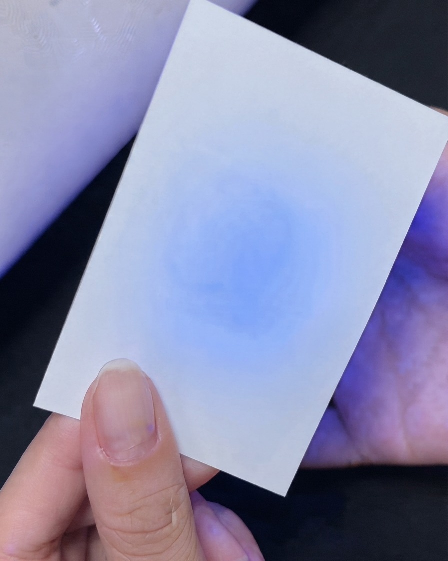 Eine Hand hält eine weiße Karte und zeigt darunter einen blauen UV-Licht-Reflexionstest.