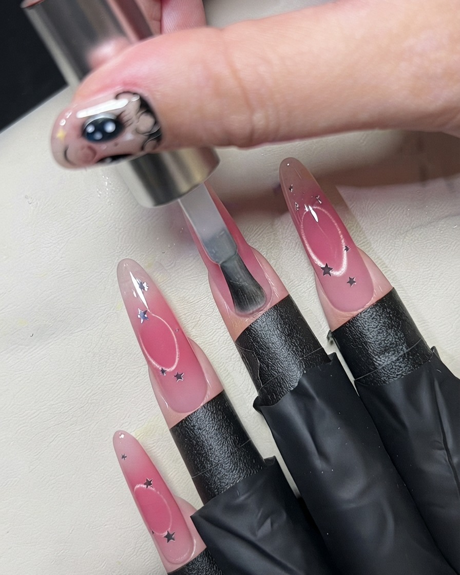 Ein Pinsel trägt einen klaren Überlack über einem mit Sternen-Pailletten verzierten Nagel auf.