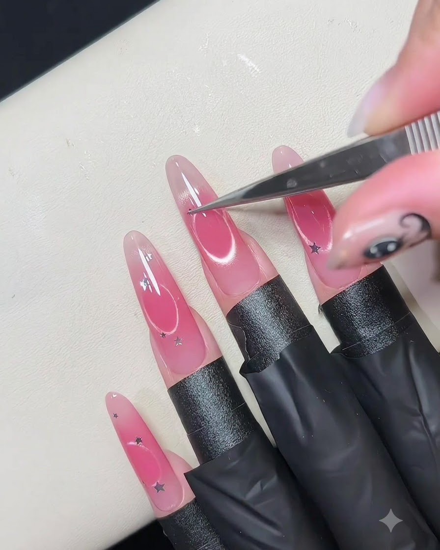 Eine feine Pinzette platziert kleine silberne Sternen-Pailletten um den Rand eines hohlen, kreisförmigen Nageldesigns.