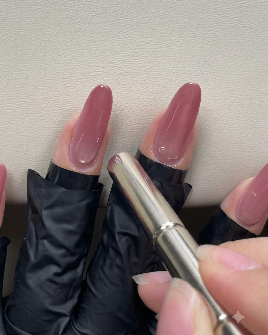 Eine Hand benutzt einen zylindrischen Stiftmagneten und hält ihn nahe an die Nagelhaut eines pfirsichrosa Gelnagels, um das magnetische Cat-Eye-Highlight zu formen.