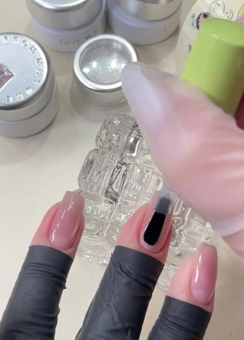 Ein Pinsel trägt klares Base Gel auf einen Nagel auf, bevor dekorative Sternen-Pailletten platziert werden.