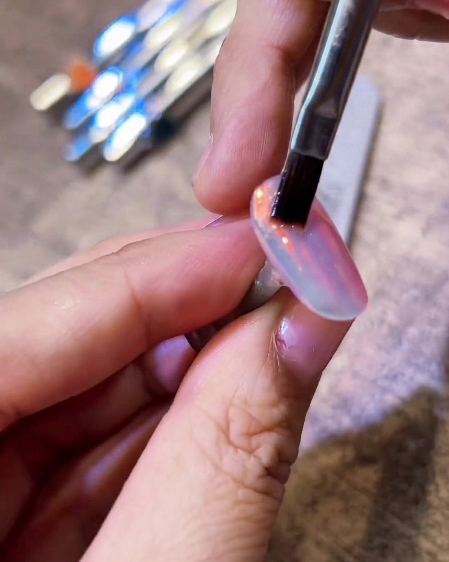 Ein flacher Borstenpinsel streicht sanft über einen glänzenden Aurora-Chromnagel, um überschüssiges Puder zu entfernen.
