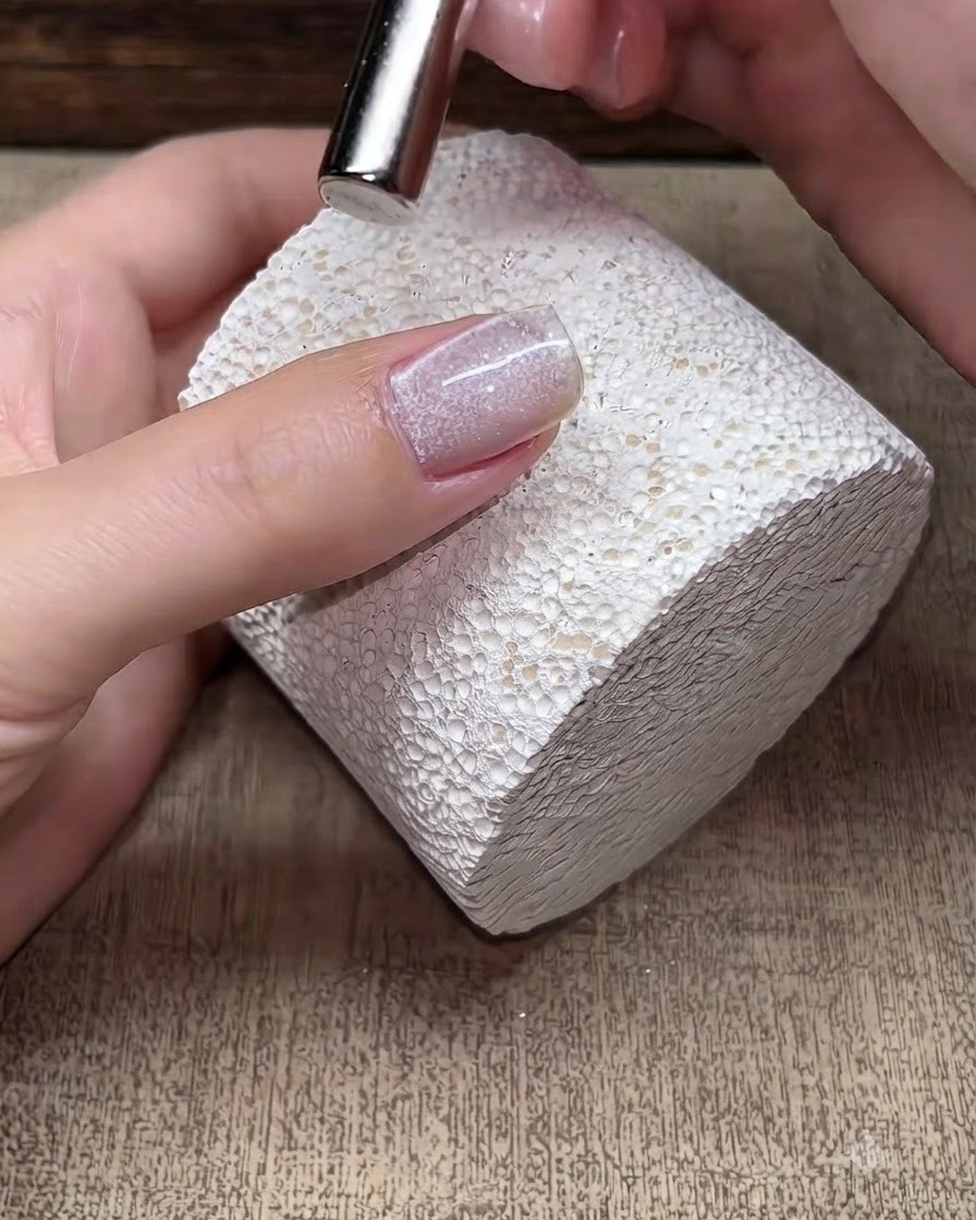 Ein kleiner Magnet schwebt über einem feuchten Cat-Eye-Gel-Nagel, um die magnetischen Schimmerpartikel zu formen.