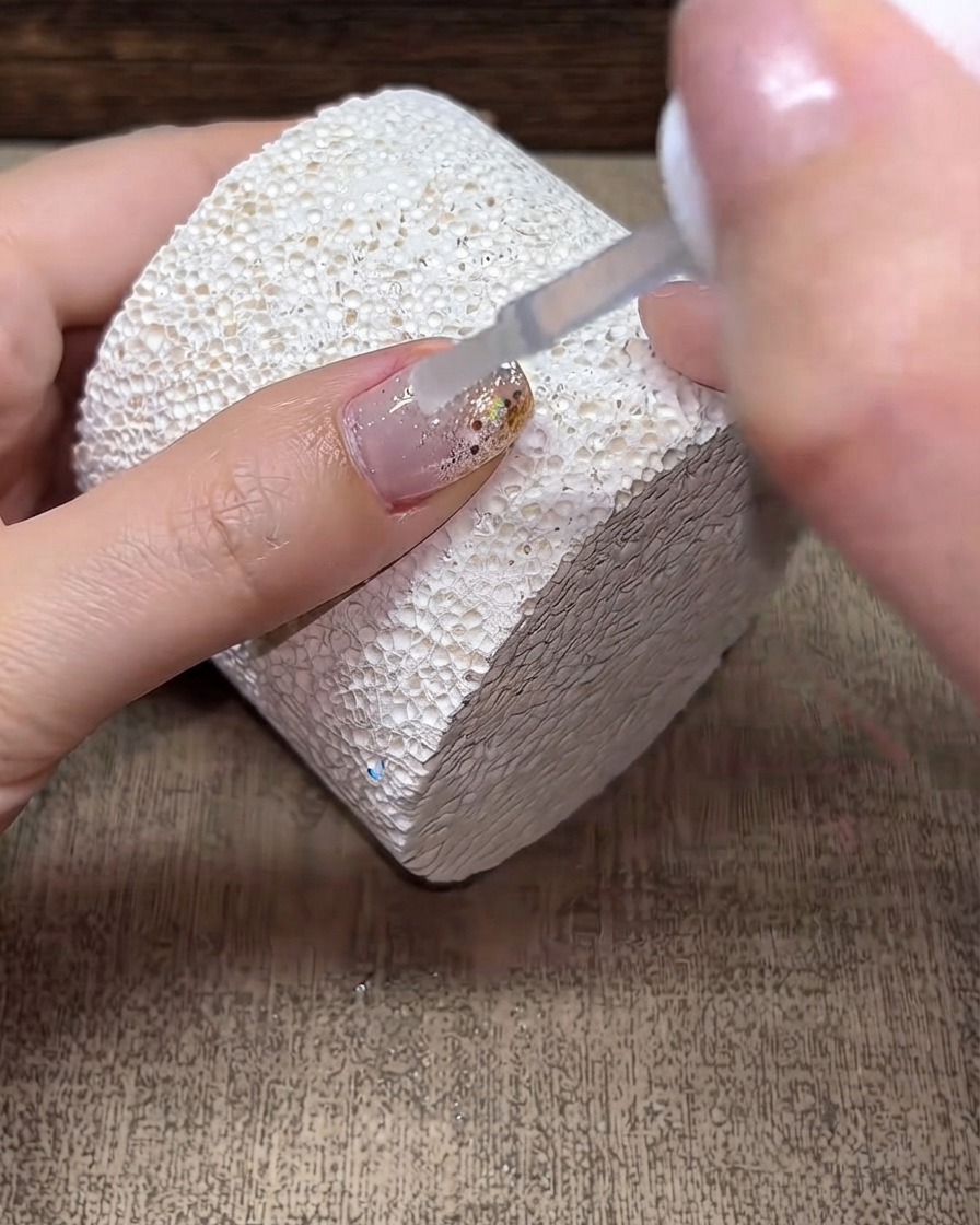 Ein Pinsel trägt eine klare Schicht Builder Gel auf eine dekorierte Nageloberfläche auf.