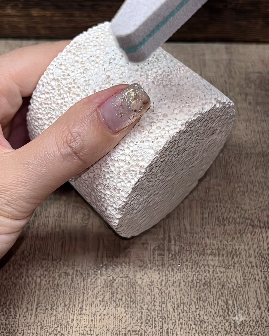 Eine Pufferfeile glättet die Oberfläche eines manikürten Fingernagels.