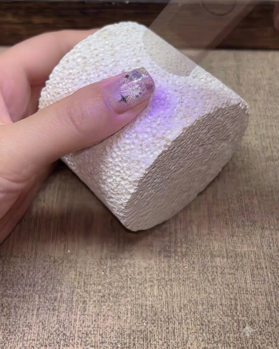 Eine Hand härtet unter einer lila UV-LED-Nagellampe aus.