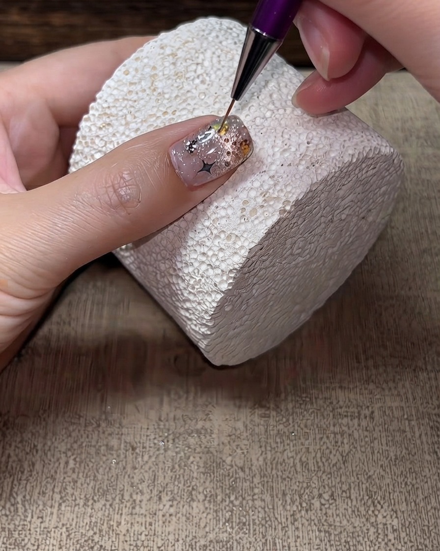 Ein feiner Liner-Pinsel trägt harten Top Coat um die Kanten und Lücken von Strasssteinen auf einem fertigen Nagel auf.