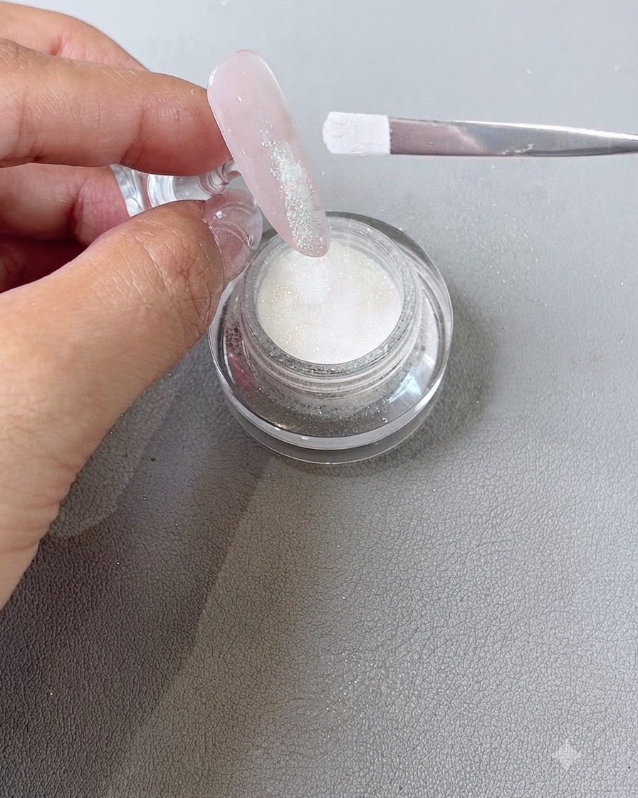 Dip-Powder wird mit einem Pinsel auf den feuchten Gel-Spitzenbereich eines Fingernagels gestreut.