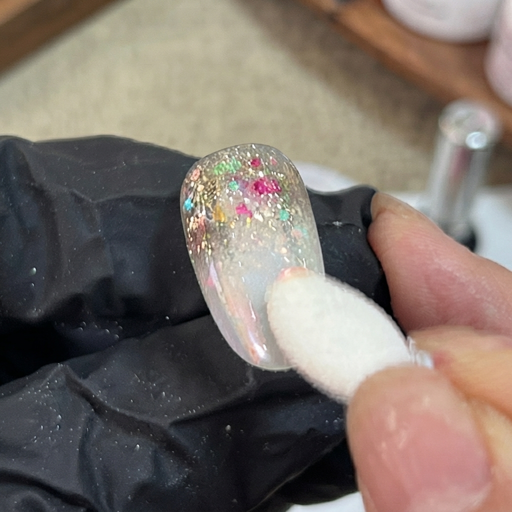 Ein Schwammapplikator tupft schillerndes Aurora-Puder auf den Verlaufsschnitt eines dekorierten künstlichen Nagels.