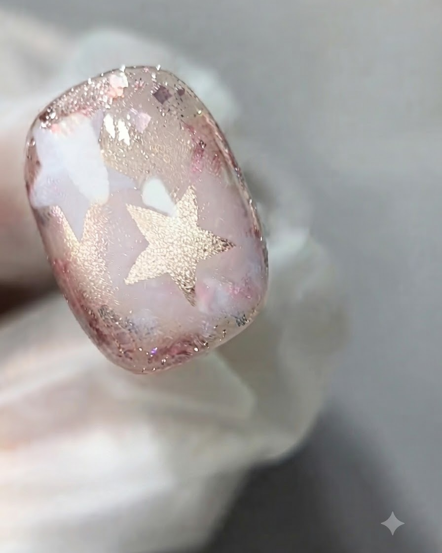 Ein Nagelpinsel trägt eine Schicht transparentes rosa Cat-Eye-Gel auf die Oberfläche eines verzierten Nagels auf.