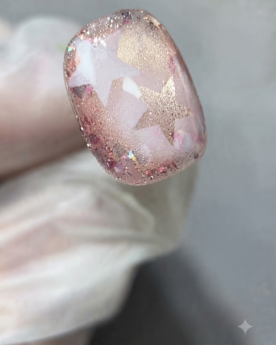 Eine Pinzette oder behandschuhte Finger ziehen eine Sternschablone vorsichtig von der ausgehärteten Nail Art ab.