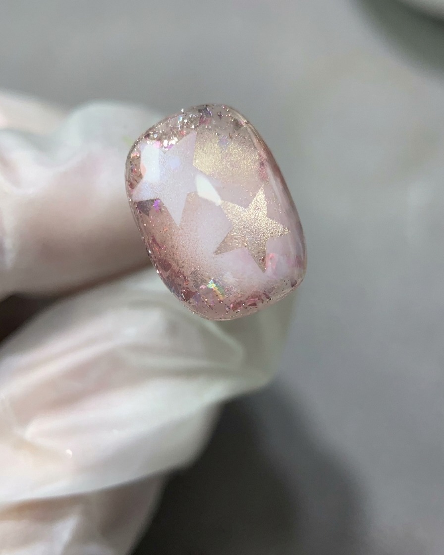 Ein Nagelpinsel verteilt eine glatte, dünne Schicht klares Basislack über dem fertigen Stern- und Glitter-Nageldesign.