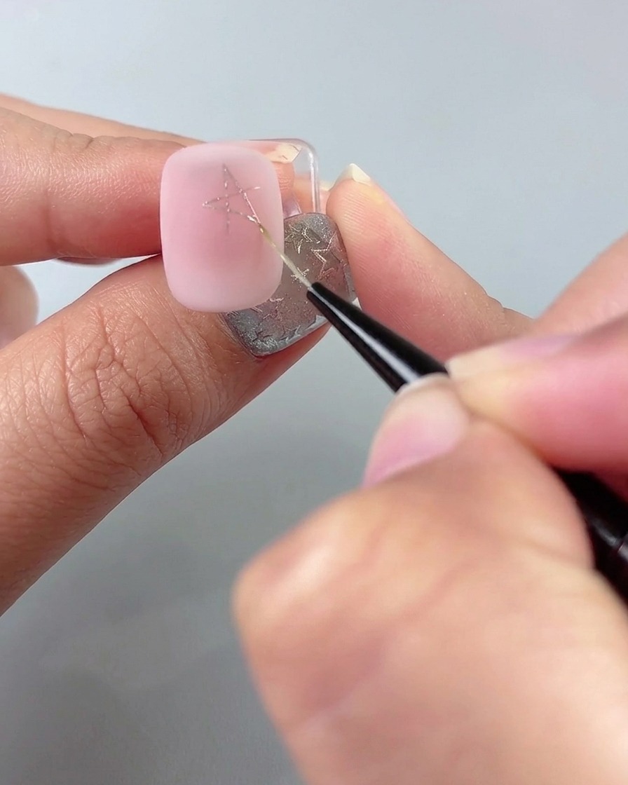 Ein feiner Liner-Pinsel zeichnet Linien, um eine Sternform auf einem rosa manikürten Nagel zu vervollständigen.