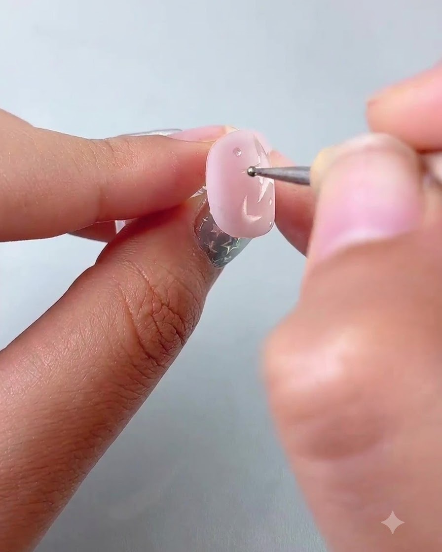 Ein Dotting-Pen platziert kleine Akzentpunkte um gemalte Sterne auf einem rosa Nagel.