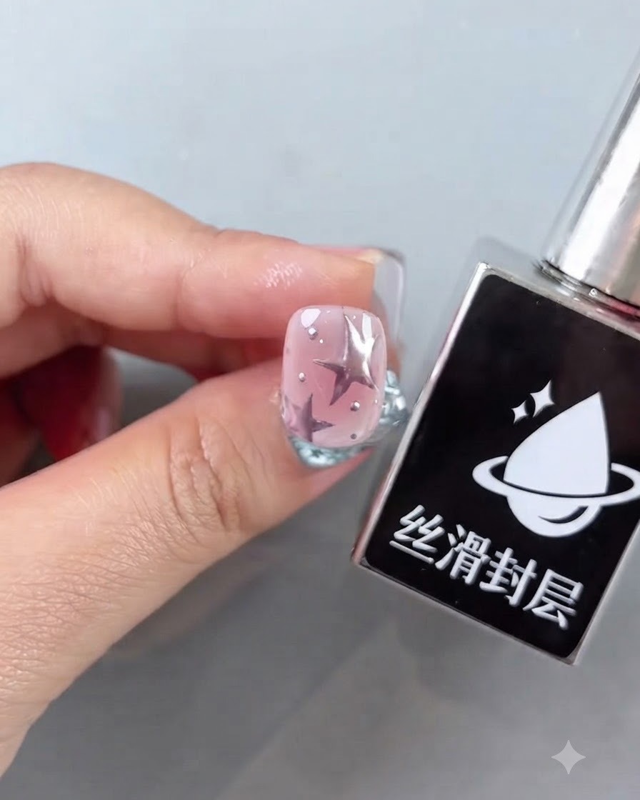 Eine Flasche glatter Top-Coat neben einem fertigen rosa Nagel mit Sternmotiven und glänzenden silbernen Akzenten.