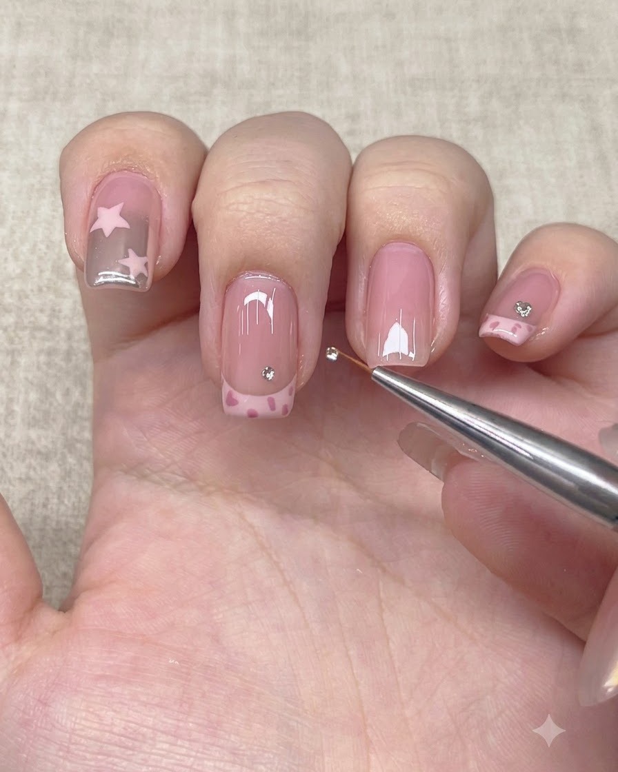 Ein Detail-Werkzeug platziert einen kleinen Strassstein oberhalb der French-Tip-Linie auf einem Nagel.