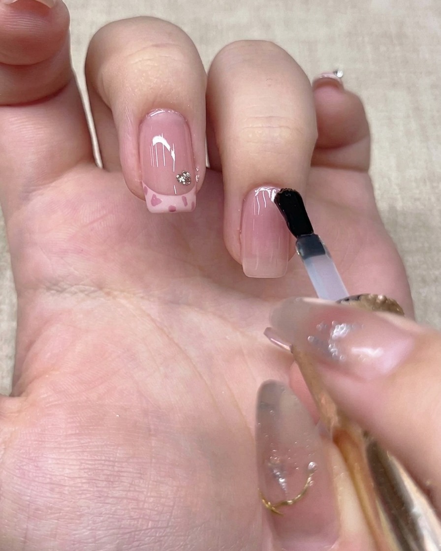 Ein Pinsel trägt einen klaren Topcoat auf den Nagel eines Ringfingers auf.