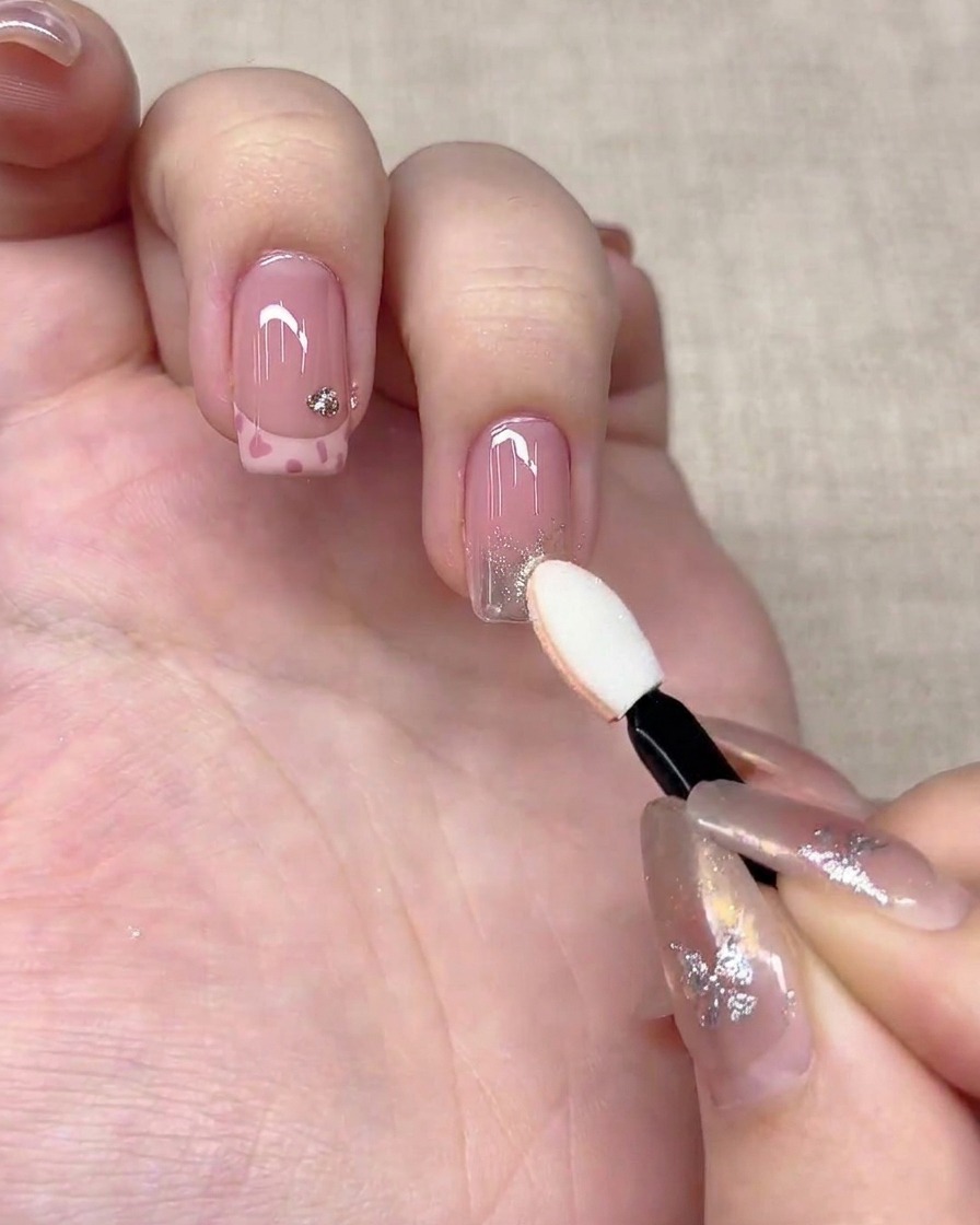 Ein Lidschatten-Schwammapplikator drückt silbernes Chrompuder auf die Spitze eines Fingernagels.