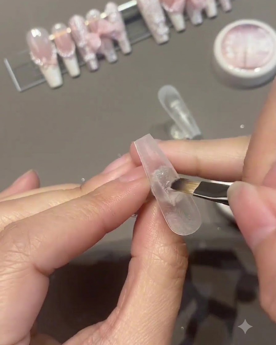 Ein Pinsel trägt eine zweite Schicht rosa Gel-Lack auf die Oberfläche eines künstlichen Nagels auf.