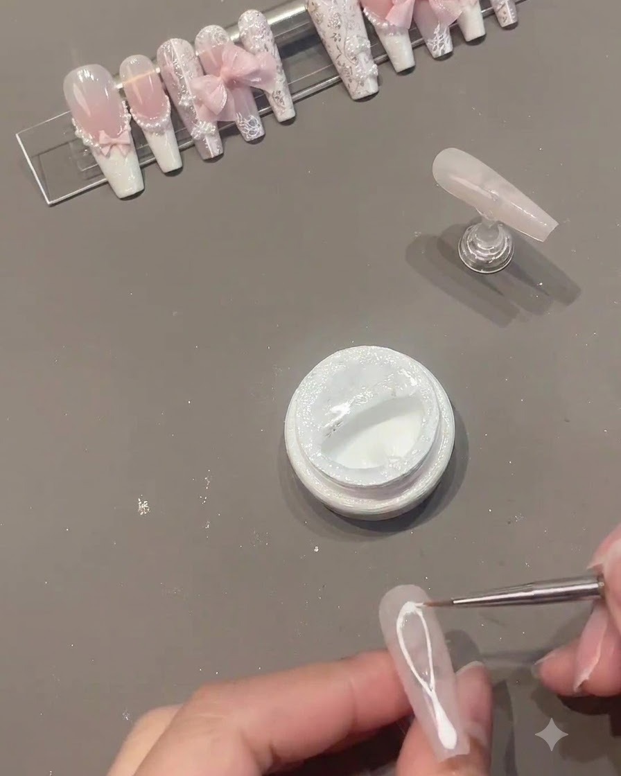 Ein feiner Liner-Pinsel zieht weiße Spider-Gel-Linien über die Mitte eines rosa Gelnagels.