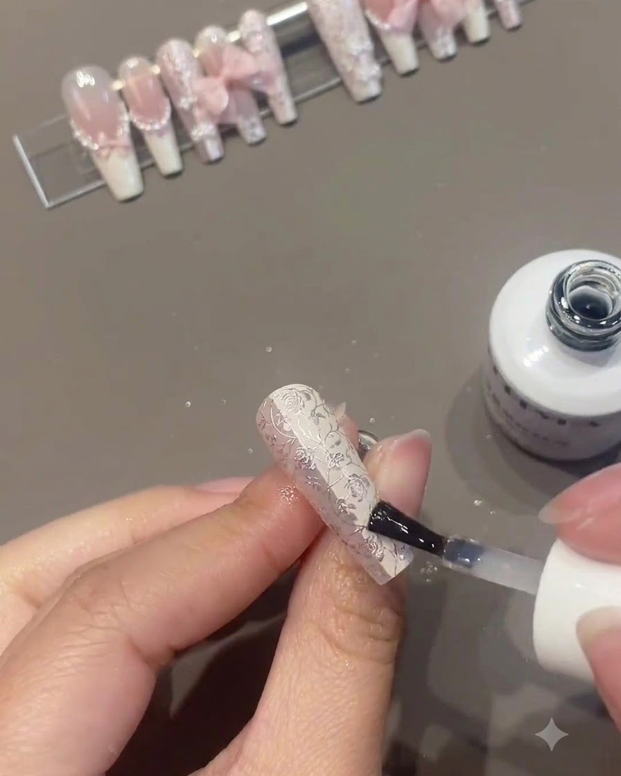 Ein Nagelpinsel trägt Klarlack oder Überzugslack auf einen kunstvoll verzierten Blumennagel auf, während andere fertige Nägel im Hintergrund auf einem Ständer präsentiert werden.